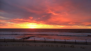 Een zonsondergang boven de oceaan, met een houten omheining op de voorgrond.