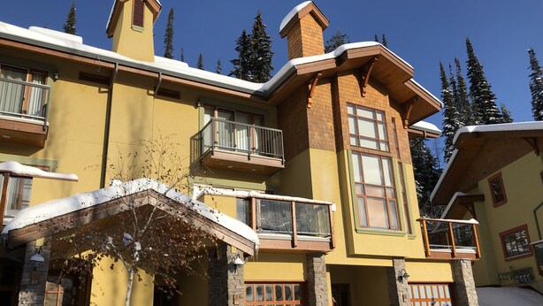 Un immeuble à plusieurs étages, doté d’une façade jaune, de détails en pierre et d’un toit recouvert de neige.
