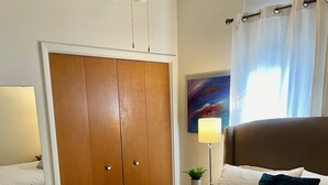 A hotel room with a large bed, a wardrobe, a ceiling fan, a nightstand with a lamp, and a painting on the wall.