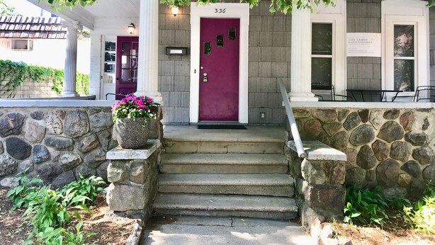 A building entrance with a purple door, stone steps, and a stone wall.