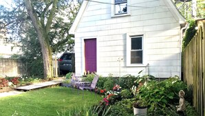 A white house with a purple door, a small garden with various plants and flowers, and a statue of a Buddha.