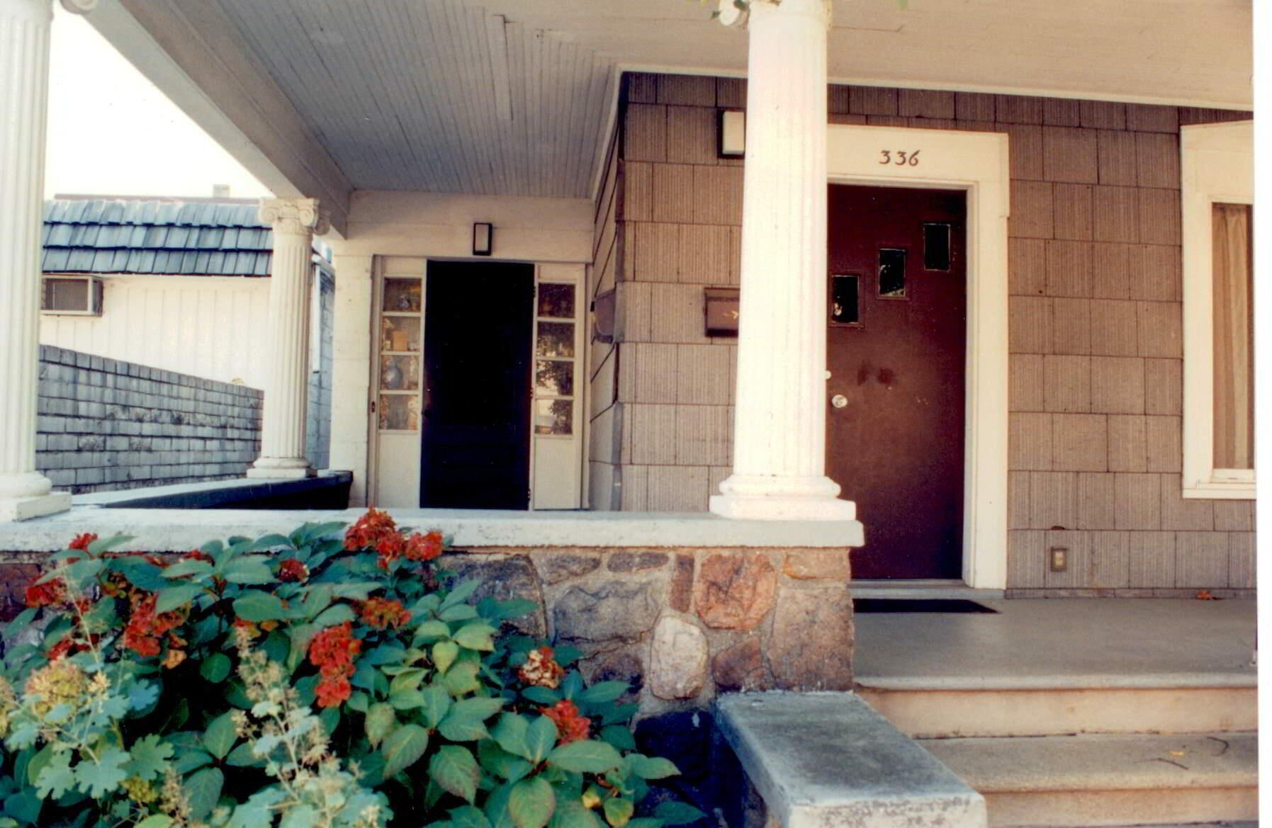 A building entrance with a dark door, a number 336 above it, and a stone wall with steps leading up to the door.