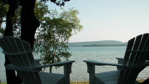 Dos sillas Adirondack mirando un lago con una orilla lejana.