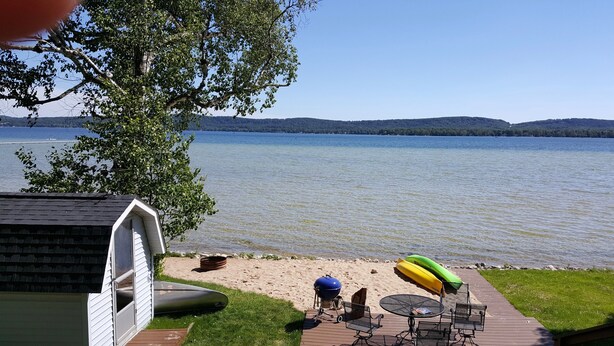 Una terraza con parrilla, asientos exteriores y kayaks junto a un lago.