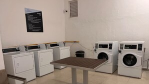 Een wasserette met meerdere wasmachines, een tafel en een stoel. Instructies zijn aan de muur bevestigd.