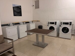 A laundry room with multiple washing machines, a table, and a chair. Instructions are posted on the wall. - Gorgeous Caribbean Ocean View (Cancún)