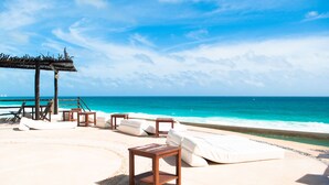 A beachside lounge with white cushioned seating and wooden tables, overlooking the ocean. - Beautiful Ocean View Condo 1 (Cancún)
