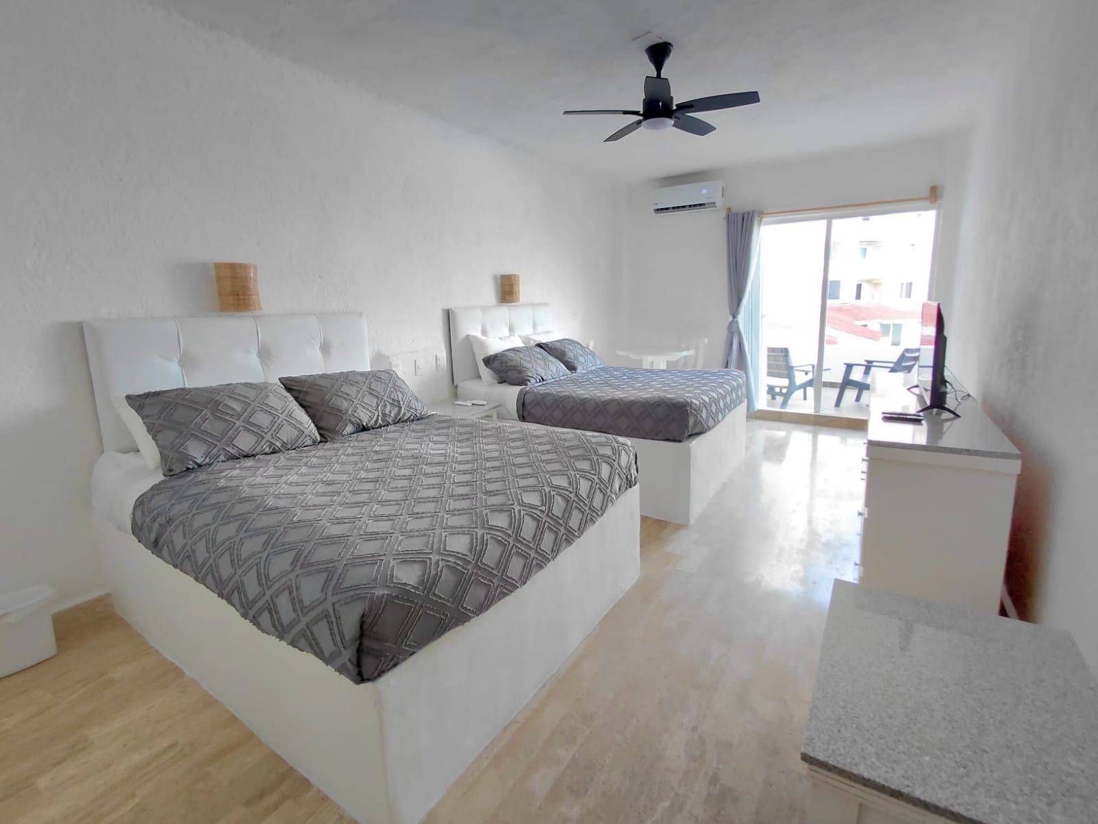 A bedroom with two beds, a ceiling fan, and a view to the outside.