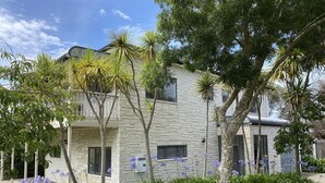 Un bâtiment à deux étages, doté d’une façade en pierre, entouré de jardins bien entretenus et de palmiers.