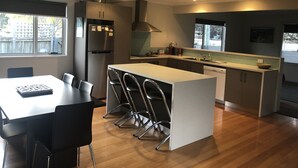 A modern kitchen with a central island, black chairs, a dining table, and a refrigerator. - Moorings - escape (Orford)