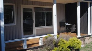 A covered porch with large sliding glass doors, a small table with chairs, and a wooden deck. - Moorings - escape (Orford)