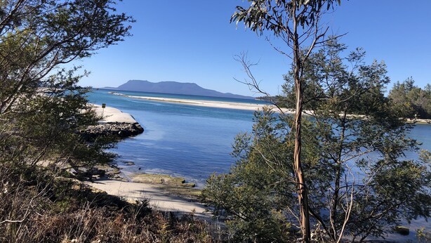A coastal landscape with clear blue waters, sandy beaches, and a mountain in the background. - Moorings - escape (Orford)