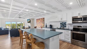 A modern kitchen with white cabinetry, a large island with bar stools, stainless steel appliances, and a view to the outdoors. - Beachfront 3 BR condo in Diamond Beach with pool - Completely renovated for 2024 (Wildwood)