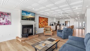 A spacious living room with a fireplace, a large painting, and a modern kitchen in the background. - Beachfront 3 BR condo in Diamond Beach with pool - Completely renovated for 2024 (Wildwood)