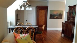 A dining area with a wooden table, four chairs, a sofa with a colorful cushion, a wooden cabinet, and a painting of a landscape. - Charming Tree Top Victorian - Two Bedroom Retreat (Boston)