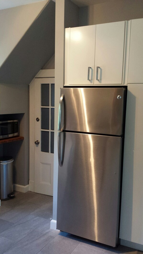 A stainless steel refrigerator in a kitchen with white cabinets and a door with frosted glass panels. - Charming Tree Top Victorian - Two Bedroom Retreat (Boston)