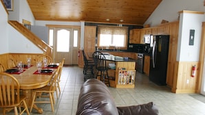 A spacious kitchen with wooden cabinets, a dining area with a wooden table and chairs, and a leather couch. - Elegant, spacious 5 bedroom home on Molasses Pond (Eastbrook)