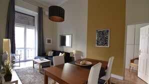 Moderni olohuone, jossa on ruokailutila. Tilaan kuuluu puinen pöytä, valkoiset tuolit, sohva ja suuri ikkuna, jossa on verhot.