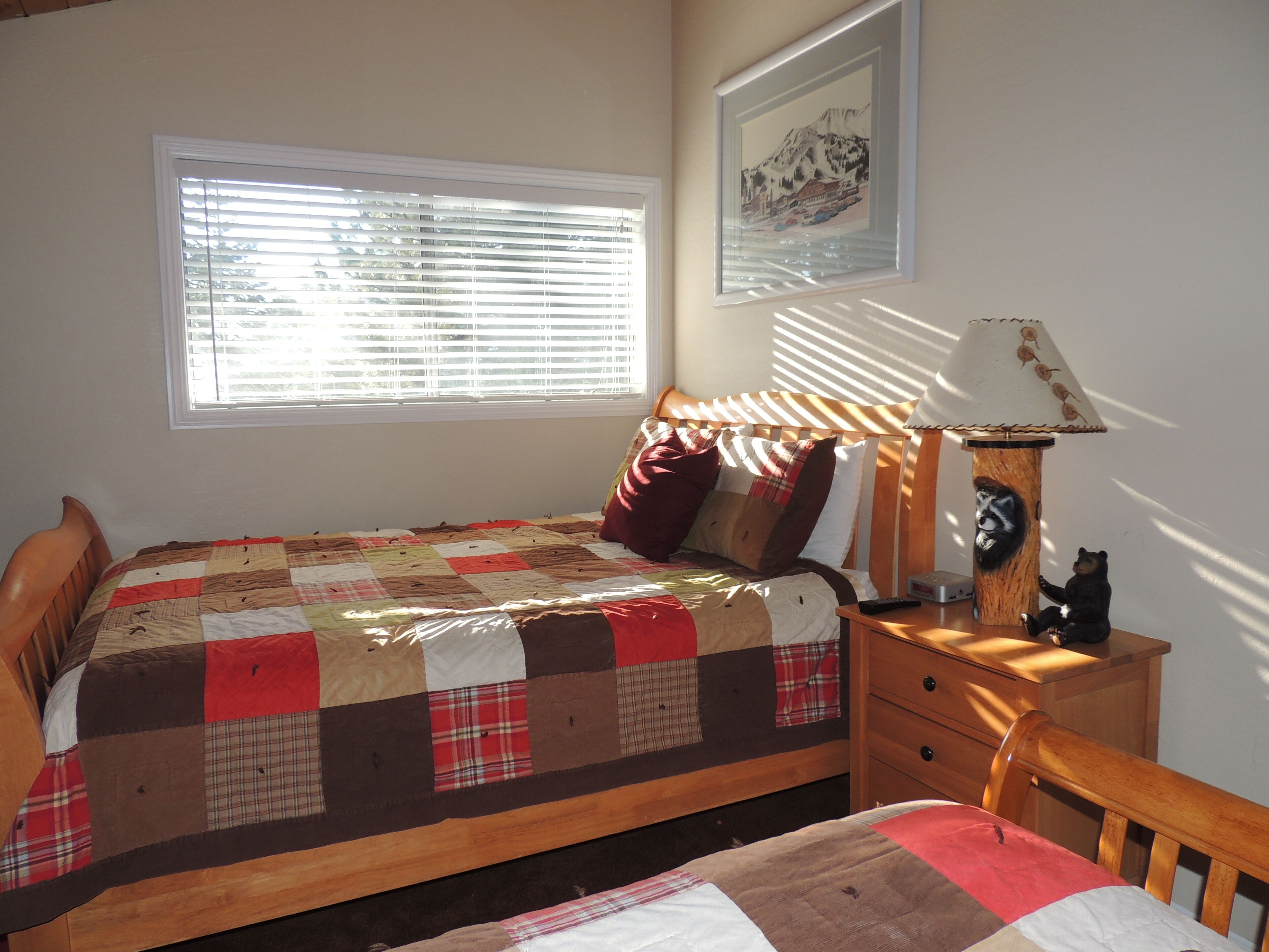 A bedroom with a wooden bed, a quilt, a nightstand with a lamp, and a framed picture on the wall.