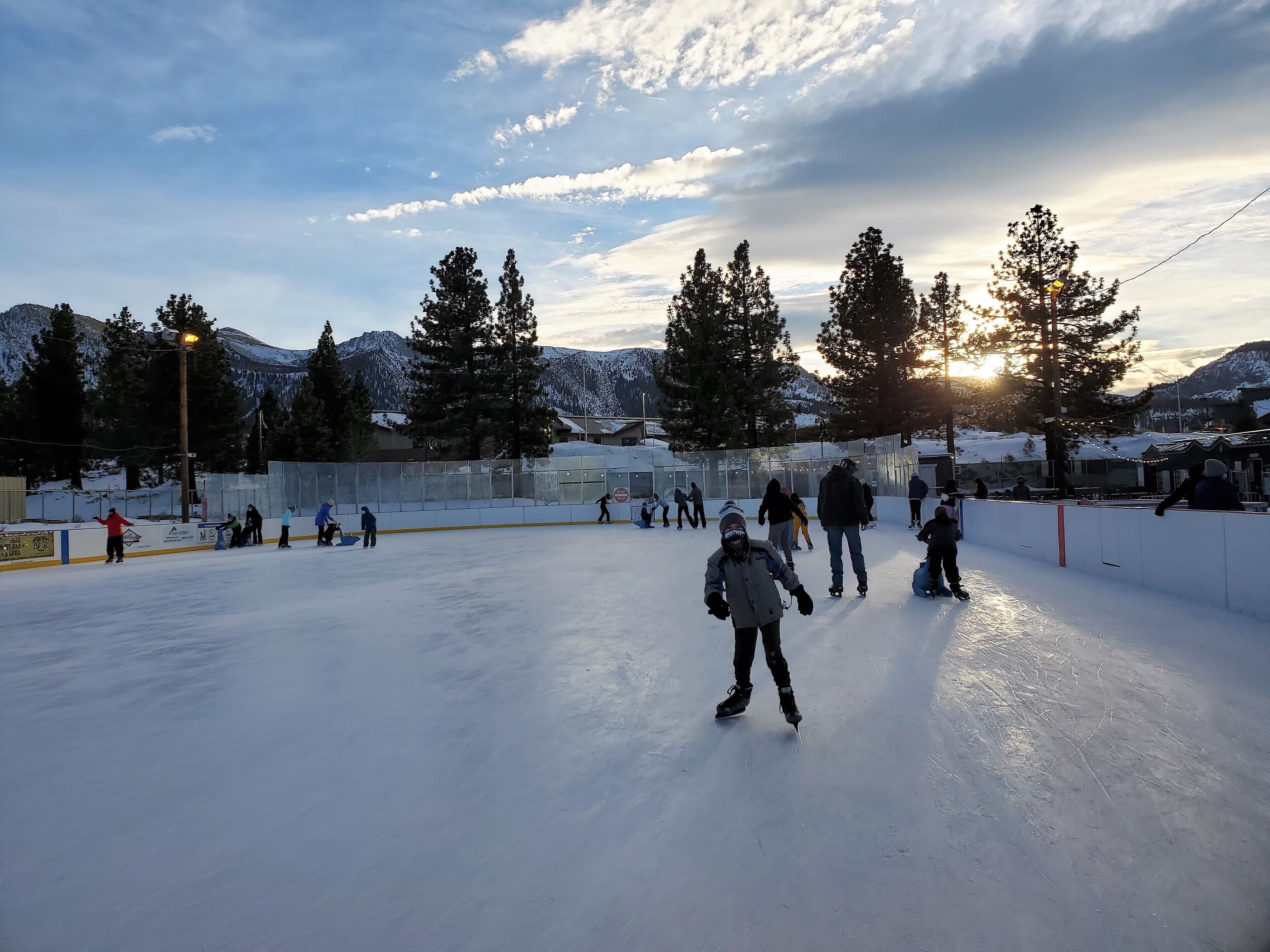 An outdoor ice skating rink surrounded by snow-covered mountains and trees.