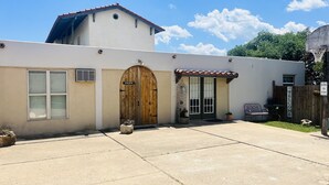 A building with a large wooden door labeled "GAME ROOM," a small fenced area with a "WELCOME" sign, and a basketball hoop. - Beautiful view,18 acres,pool, game room,Axis deer, 3 mile’s to the  river trail! (Kerrville)