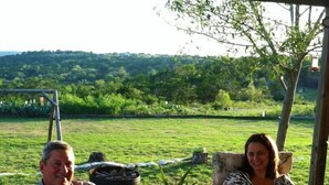 A man and a woman seated on outdoor patio furniture with a view of a green landscape. - Beautiful view,18 acres,pool, game room,Axis deer, 3 mile’s to the  river trail! (Kerrville)