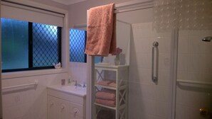 A bathroom with a window, a sink, a mirror, a shower, and a towel rack. - Butterfly Cottage - Pet Friendly Tumut (Tumut)