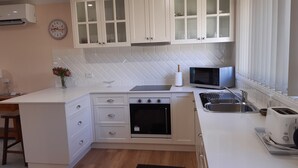 A compact kitchen with white cabinetry, a microwave, a toaster, and a sink. - Butterfly Cottage - Pet Friendly Tumut (Tumut)