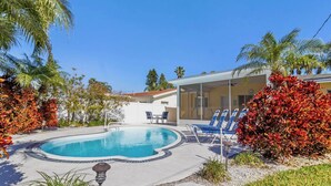 Piscina com espreguiçadeiras, rodeada por palmeiras e uma casa com varanda coberta.
