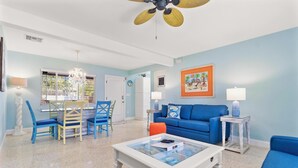 Uma sala de estar com um sofá azul, uma mesa de centro e um espaço de jantar com cadeiras azuis e um lustre.