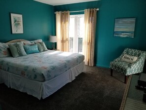 A bedroom with a large bed, a chair, a window with curtains, and a painting on the wall. - GULF VIEW LUXURIOUS CONDO,BEACH SERVICE,10% WEEKLY/MEMBER DISC. TENNIS/PICKLE CT (Okaloosa Island)
