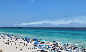 A beach with umbrellas, people, and a pier in the background.