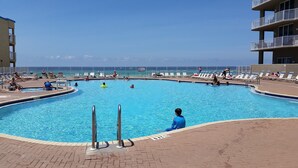 Una amplia piscina al aire libre con vista despejada al océano, rodeada de sillones de descanso y un solárium de ladrillo.