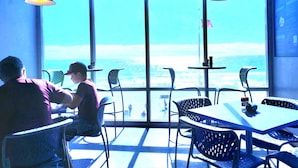 A restaurant with large windows overlooking the ocean, metal chairs, and tables.