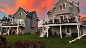 Two two-story houses with balconies, a grassy yard, and a sunset sky.