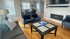 A modern living room with a sofa, two armchairs, a coffee table, and a TV mounted on the wall.