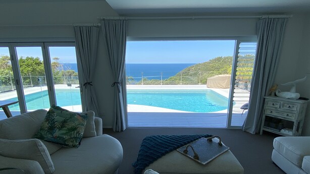 A spacious living room with a large window overlooking a pool and ocean view.