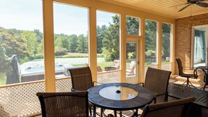 A covered patio with wicker chairs and a glass table, large windows offering a view of a hot tub and trees. - 8-Person House with Private Hot Tub on Spectacular Rural Estate (Castleton)