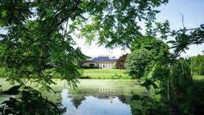 A house with a solar panel roof, surrounded by lush greenery and a pond. - 8-Person House with Private Hot Tub on Spectacular Rural Estate (Castleton)