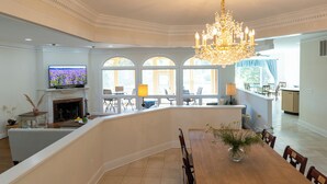 A spacious living room with a large chandelier, a fireplace, and a dining area with a wooden table and chairs. - 8-Person House with Private Hot Tub on Spectacular Rural Estate (Castleton)