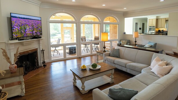 A spacious living room with a fireplace, a television, and a large window with arched tops. - 8-Person House with Private Hot Tub on Spectacular Rural Estate (Castleton)