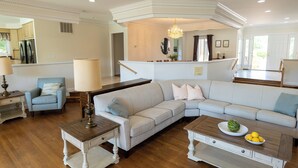 A spacious living room with a large sectional sofa, a wooden coffee table, and a dining area with a chandelier. - 8-Person House with Private Hot Tub on Spectacular Rural Estate (Castleton)