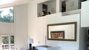 Un salon moderne avec un canapé, une table basse et un banc. Une grande fenêtre laisse entrer la lumière naturelle et offre une vue sur l’extérieur.