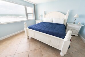A bedroom with a large window offering a view of the ocean, a white four-poster bed, and two bedside tables with lamps. - Beachfront 2BR Condo w/ Balcony & Heated Pool, Unit 224 (Satellite Beach)