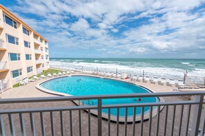 A swimming pool with a view of the ocean, surrounded by a building with multiple balconies. - Beachfront 2BR Condo w/ Balcony & Heated Pool, Unit 224 (Satellite Beach)
