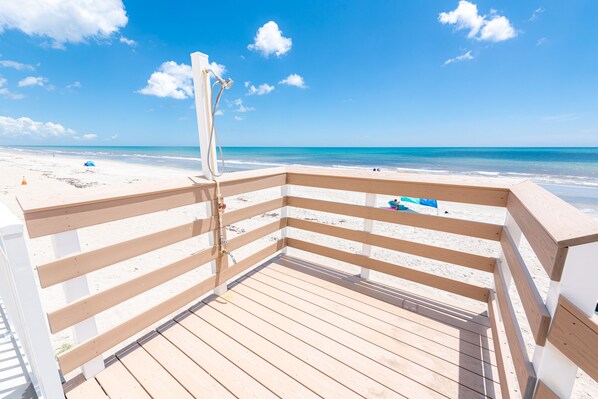 Una terraza de madera con barandal blanco que da a una playa.