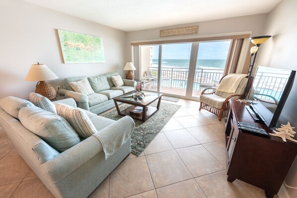 A living room with a sofa, armchairs, a coffee table, and a TV. There is a balcony with a view of the ocean. - Beachfront 2BR Condo w/ Balcony & Heated Pool, Unit 224 (Satellite Beach)
