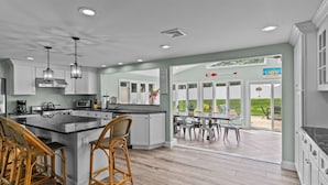 Une cuisine moderne avec des meubles blancs, un grand îlot central doté de tabourets, et une vue sur un espace patio extérieur.
