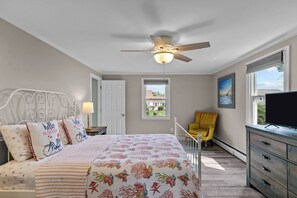 Une chambre à coucher avec un lit, un ventilateur de plafond, une fenêtre, une chaise et un téléviseur.