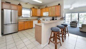 A modern kitchen with wooden cabinets, stainless steel appliances, and a bar stool area. - Large Beach View House in Surfside, South Carolina (Surfside Beach)
